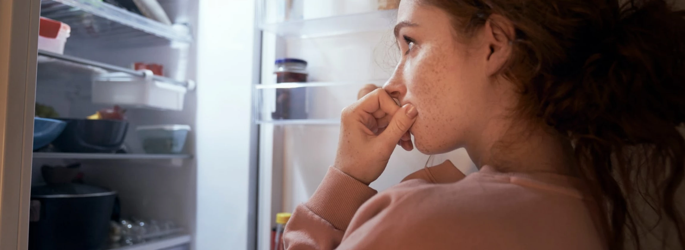 Undecided young caucasian woman checking fridge for some food at night