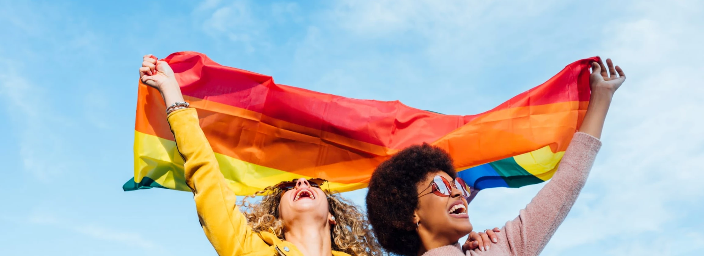 Two women friends hanging out in the city waving LGBT with pride flag