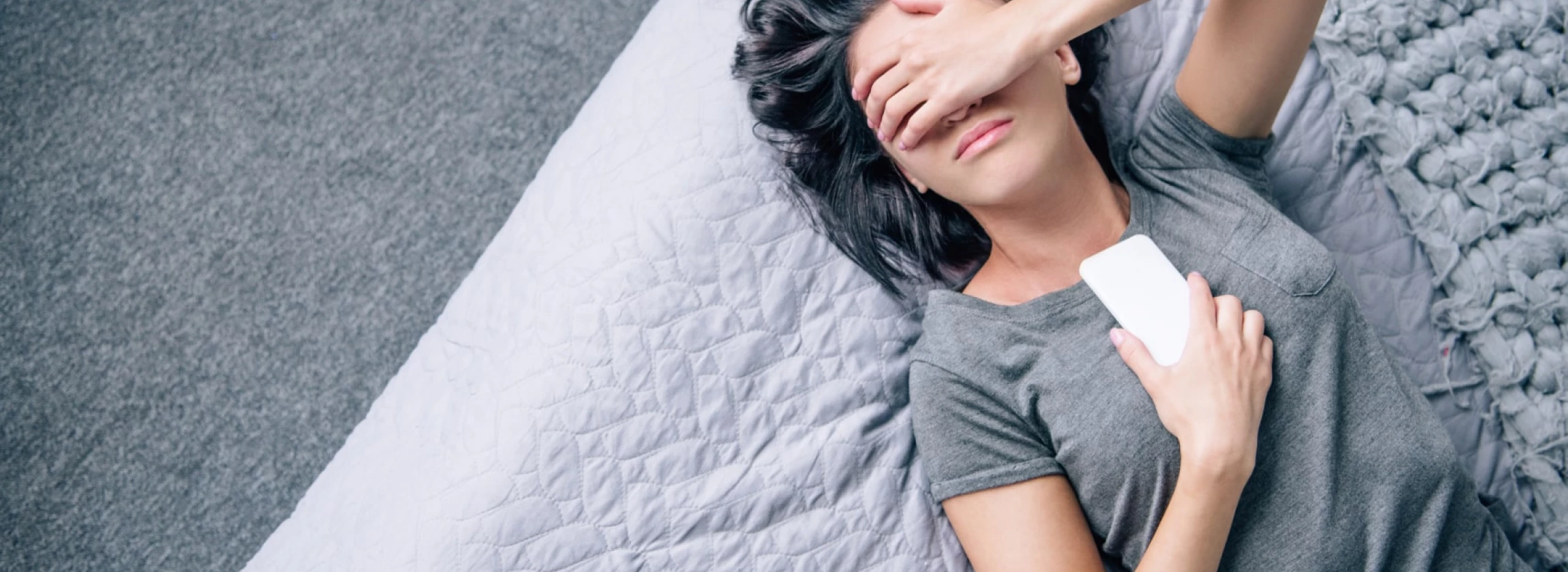 Top view of lonely depressed woman on bed with smartphone in bedroom