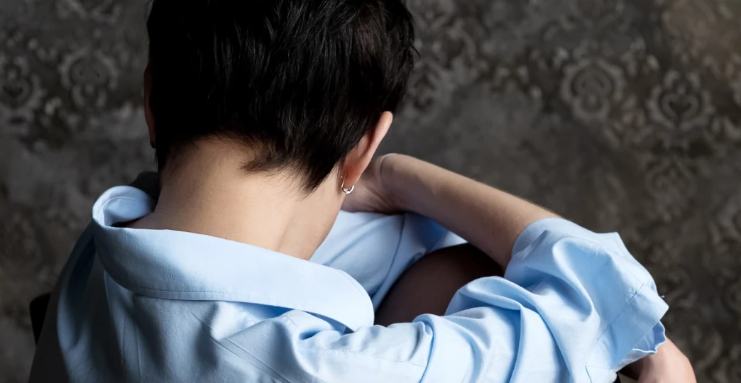 sad woman sits with her head bowed to her knees