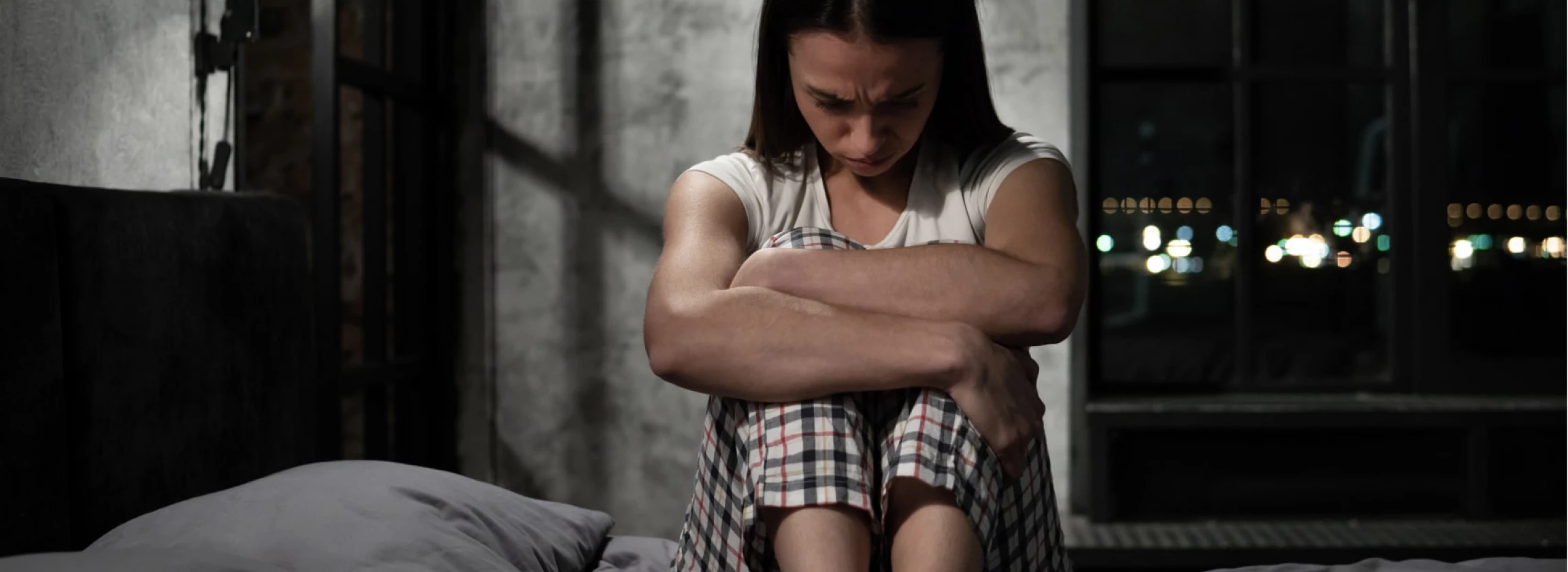 depressed young awake woman sitting alone on bed in her bedroom feeling hopeless