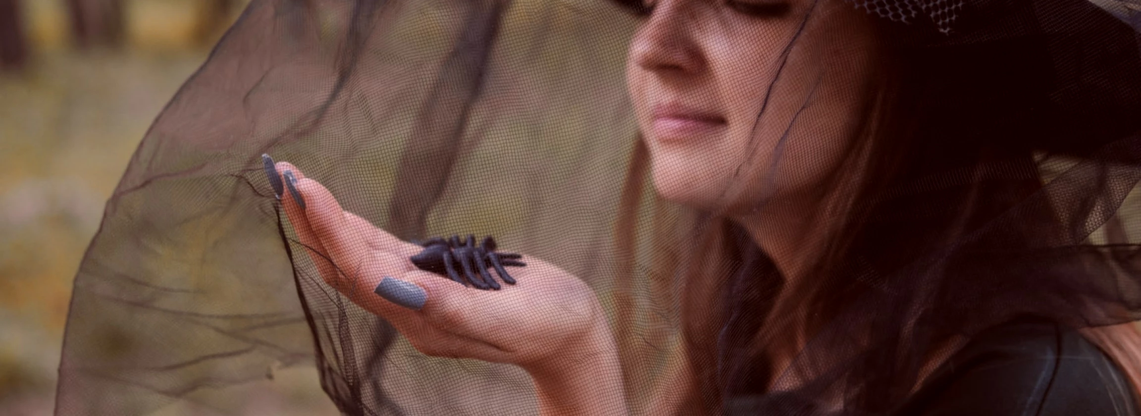 young attractive woman in a dark gown and a witchs cap clutches a black spider in her hands