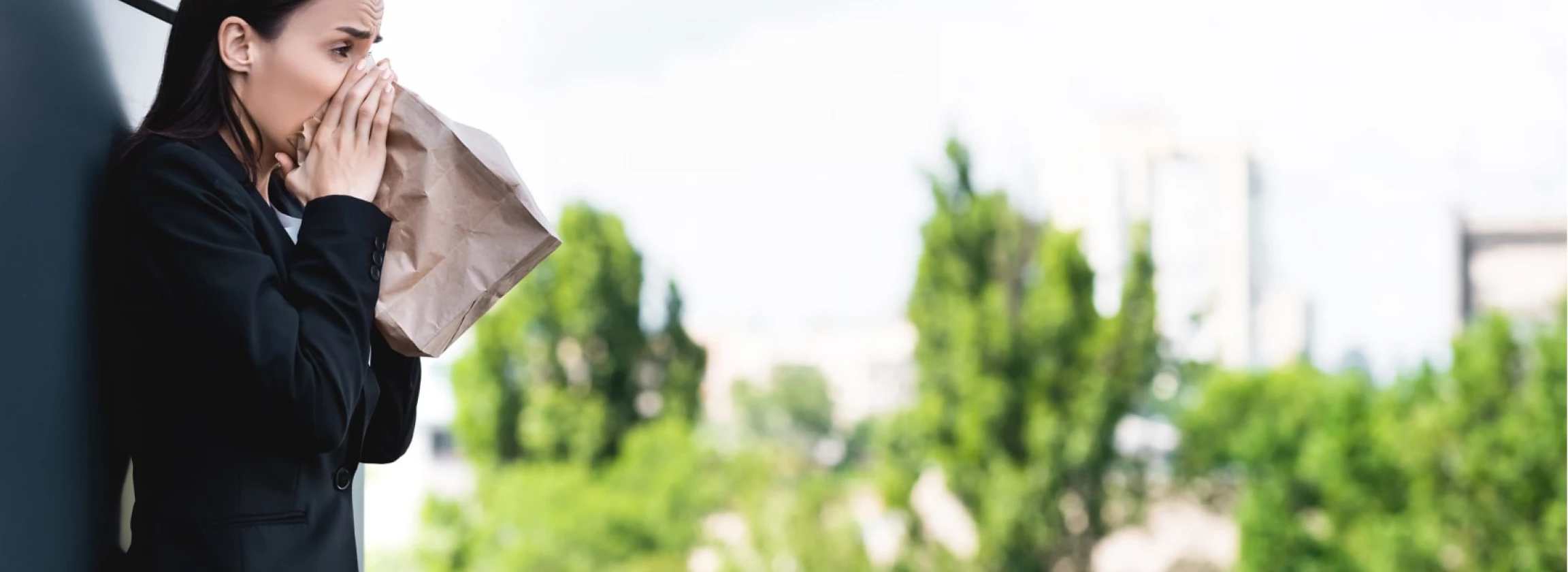 young businesswoman standing on rooftop and breathing into paper bag while suffering from panic
