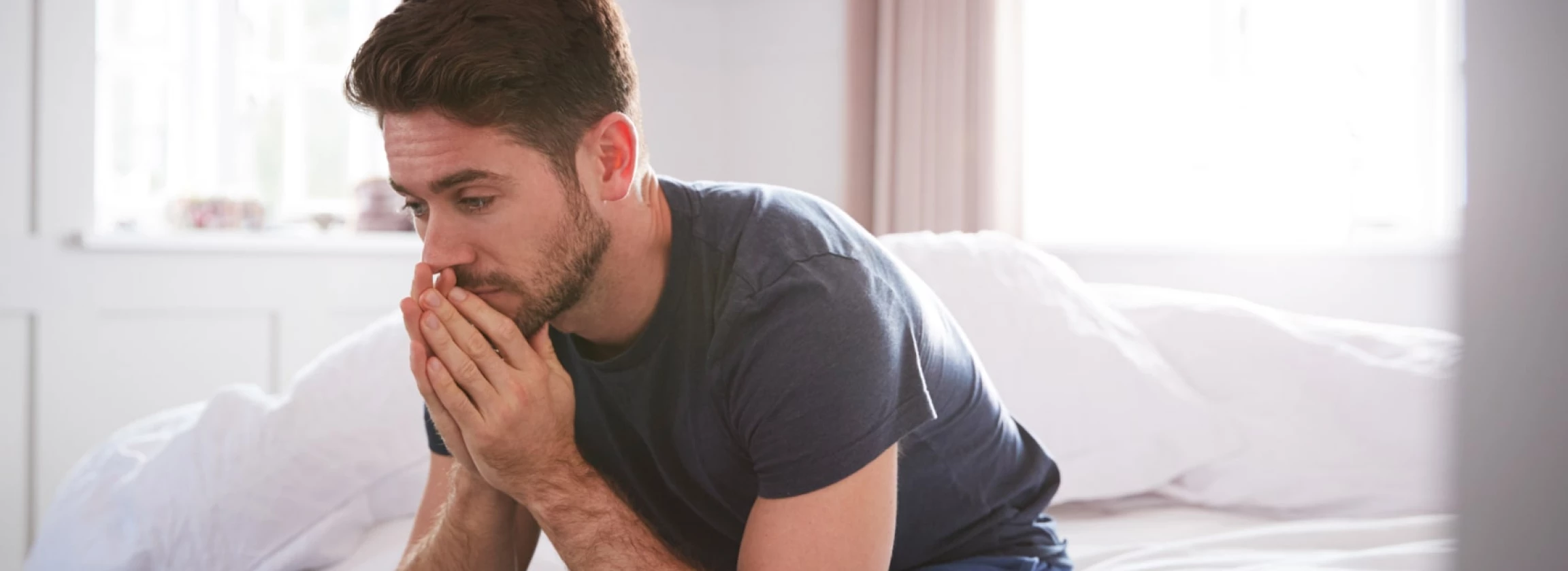 man wearing pajamas suffering with depression sitting on bed at home