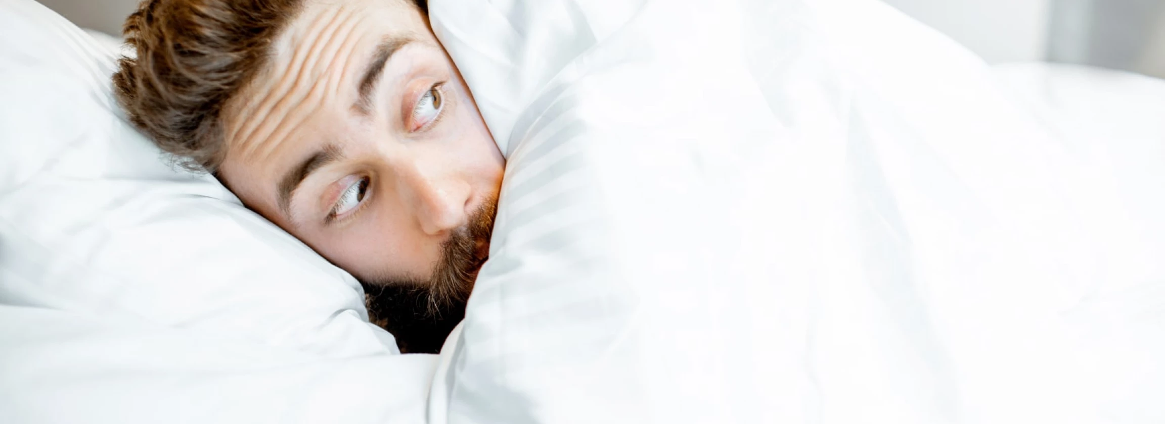 scared man hiding under the bedsheets