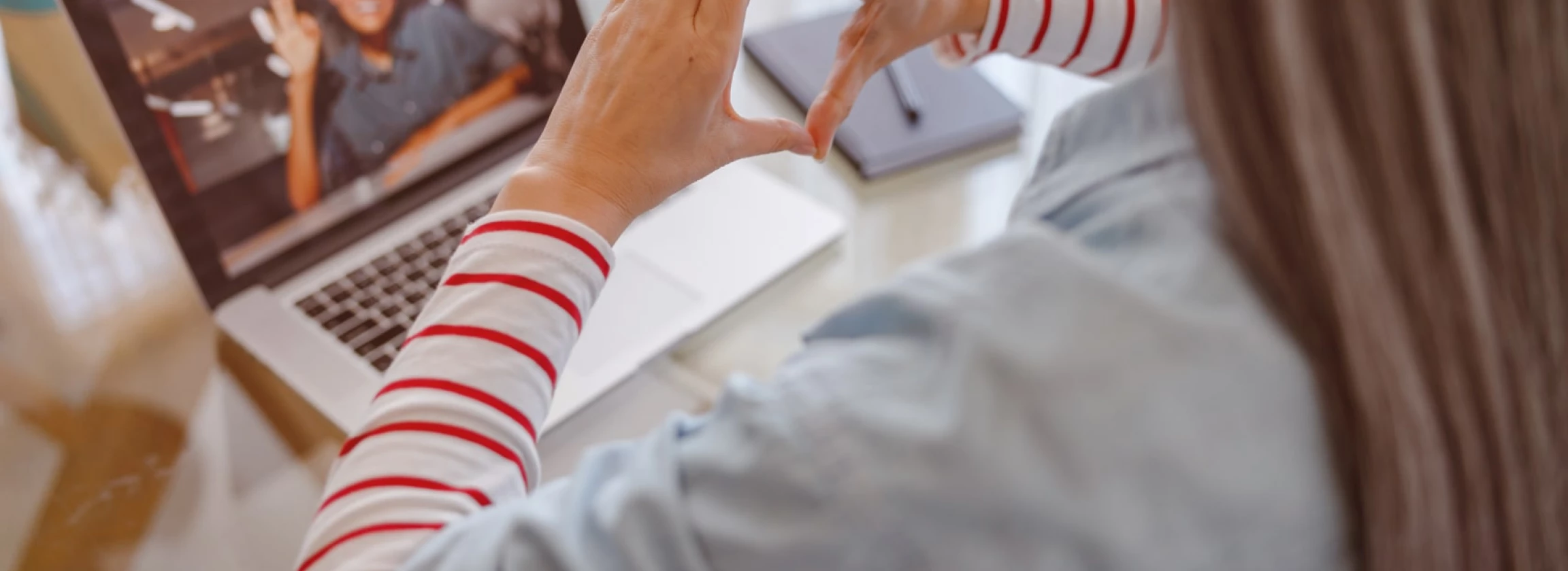 woman doing hand heart gesture while talking with therapist online