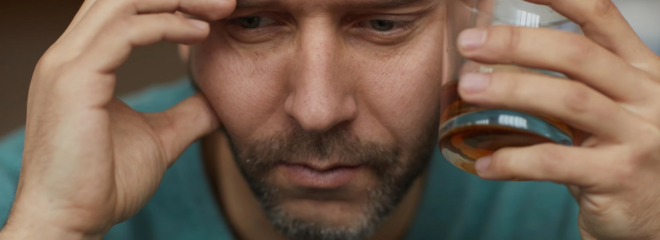Guy in his 30s/40s holding a bottle of hard liquor, looking like he’s questioning his life choices