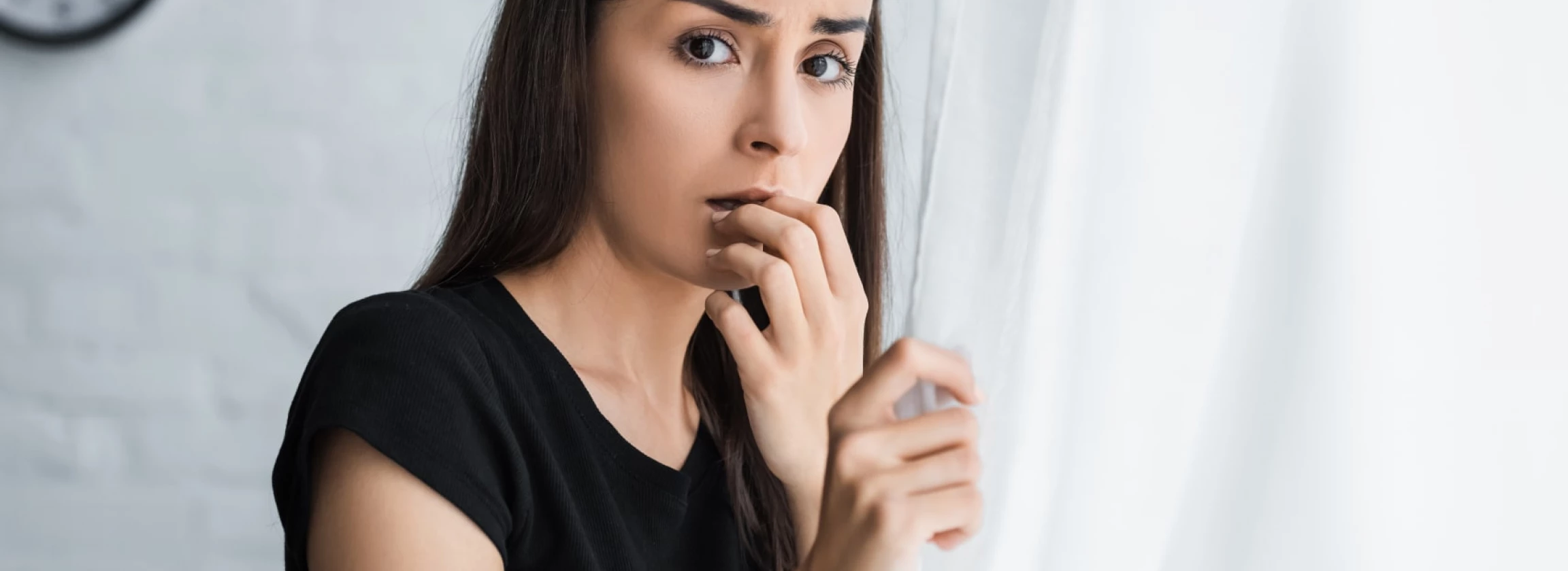 scared young woman looking at camera while standing by window and suffering from panic attack